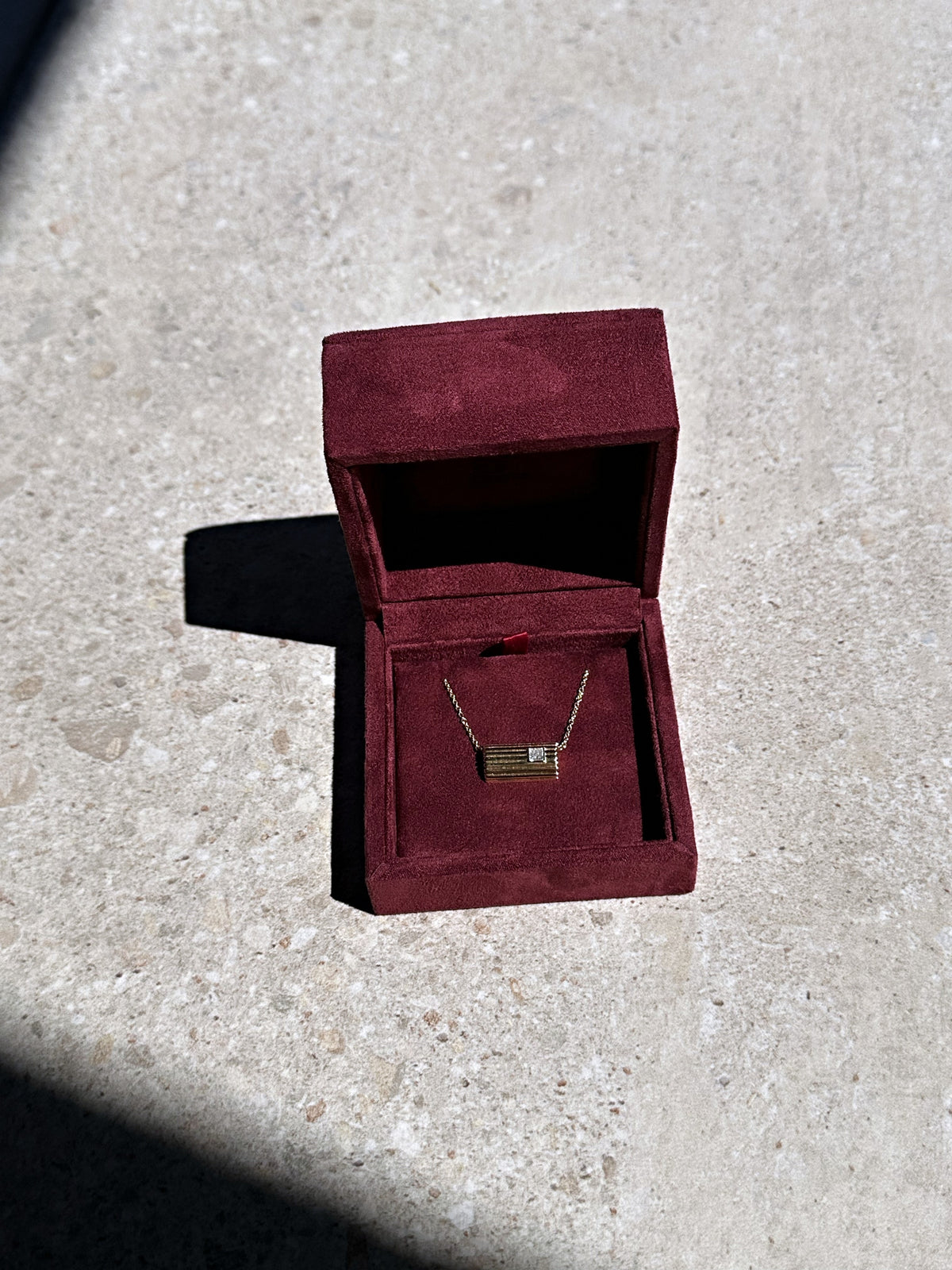 Lettre Douce necklace in its burgundy suede box, in sunlight