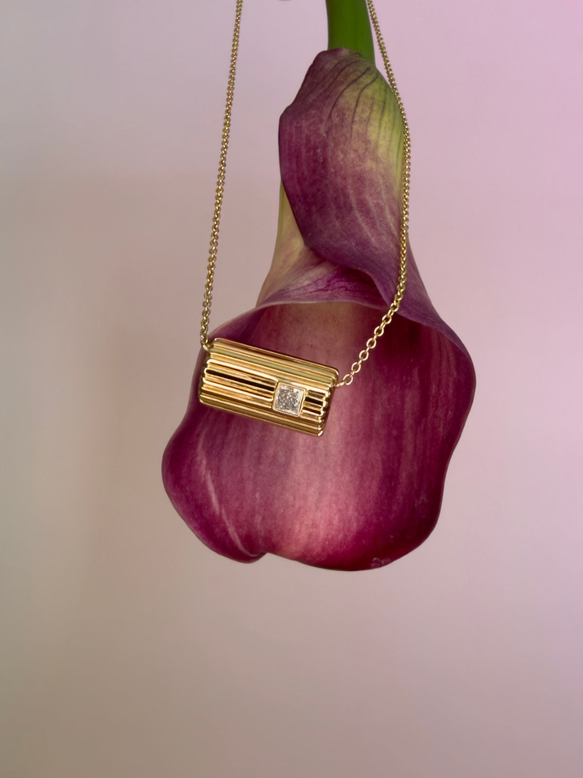 Lettre Douce necklace in solid 18k yellow gold with a princess-cut diamond, draped over a burgundy calla lily